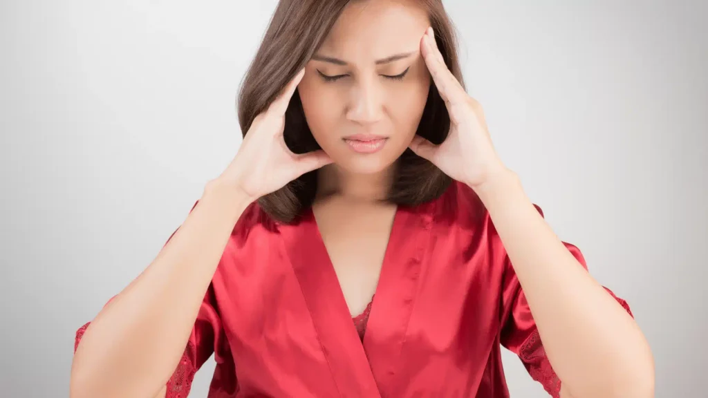 Woman wearing a red robe holding her head from tension pain and headache