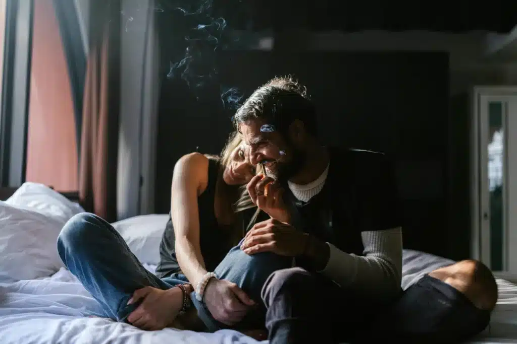 couple sitting on a bed with a lit pre-roll