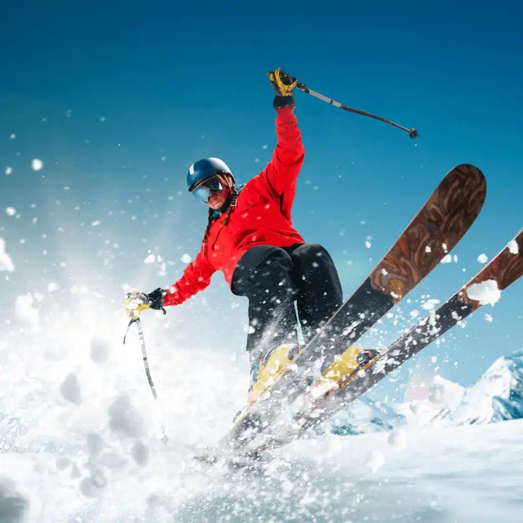 A skier in a red jacket launching off a snow jump against a clear blue sky.