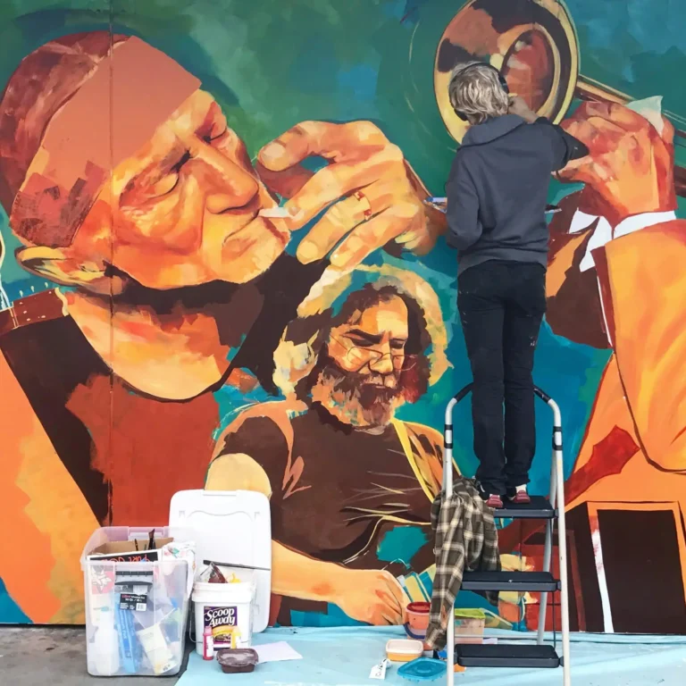 Paint supplies and a step ladder set up in front of a colorful Willie Nelson wall mural.