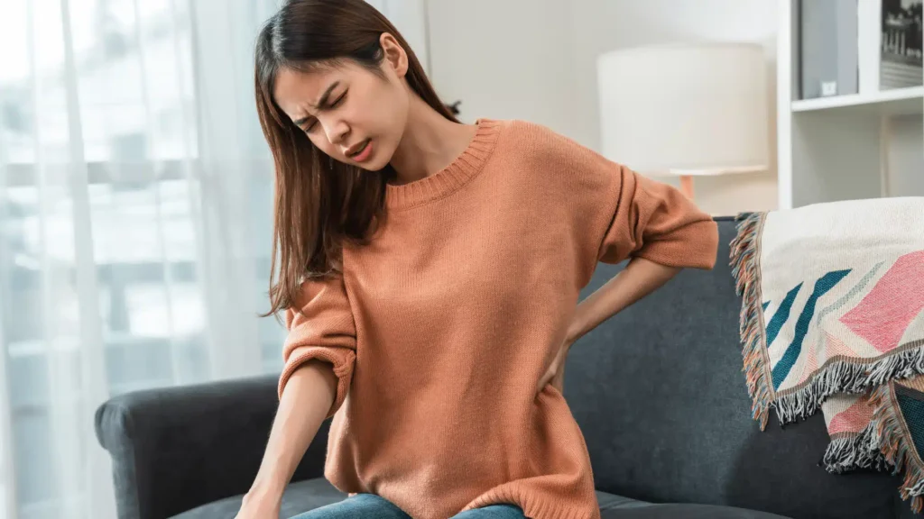 Woman sitting on a sofa holding her lower back in pain and discomfort