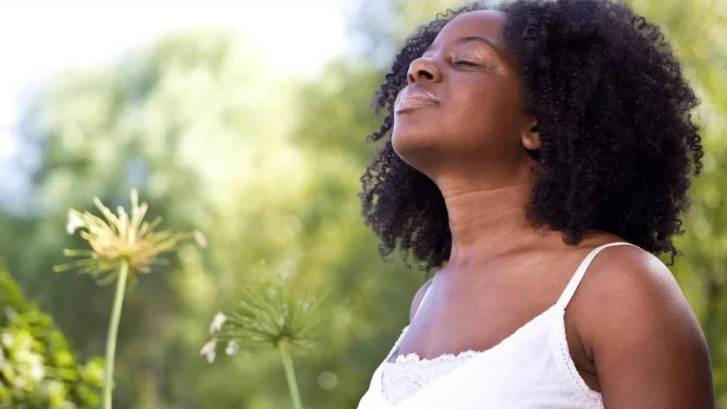 Woman standing peacefully outdoors among white wildflowers, looking relaxed and content