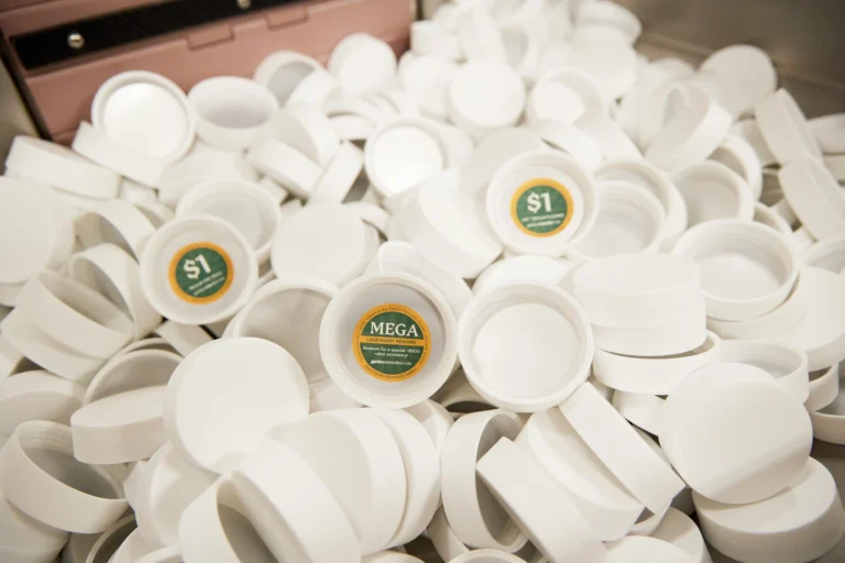 pile of many white 3.5g flower dram caps and three with winning stickers